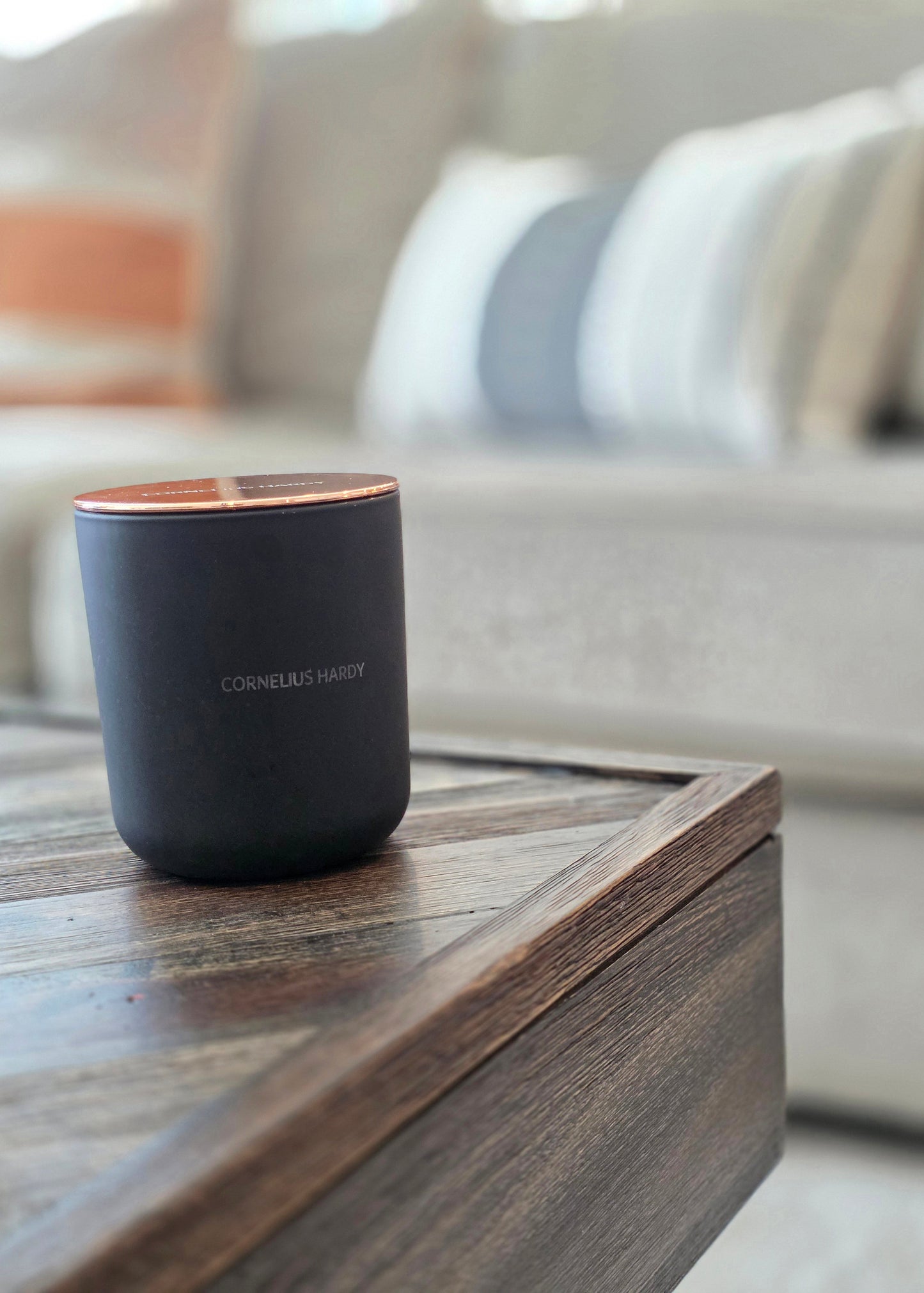 Black candle with copper rim on a wooden coffee table in a living room setting