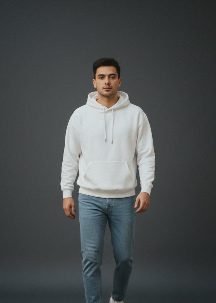 Man wearing a white hoodie and blue jeans standing against a dark gray background