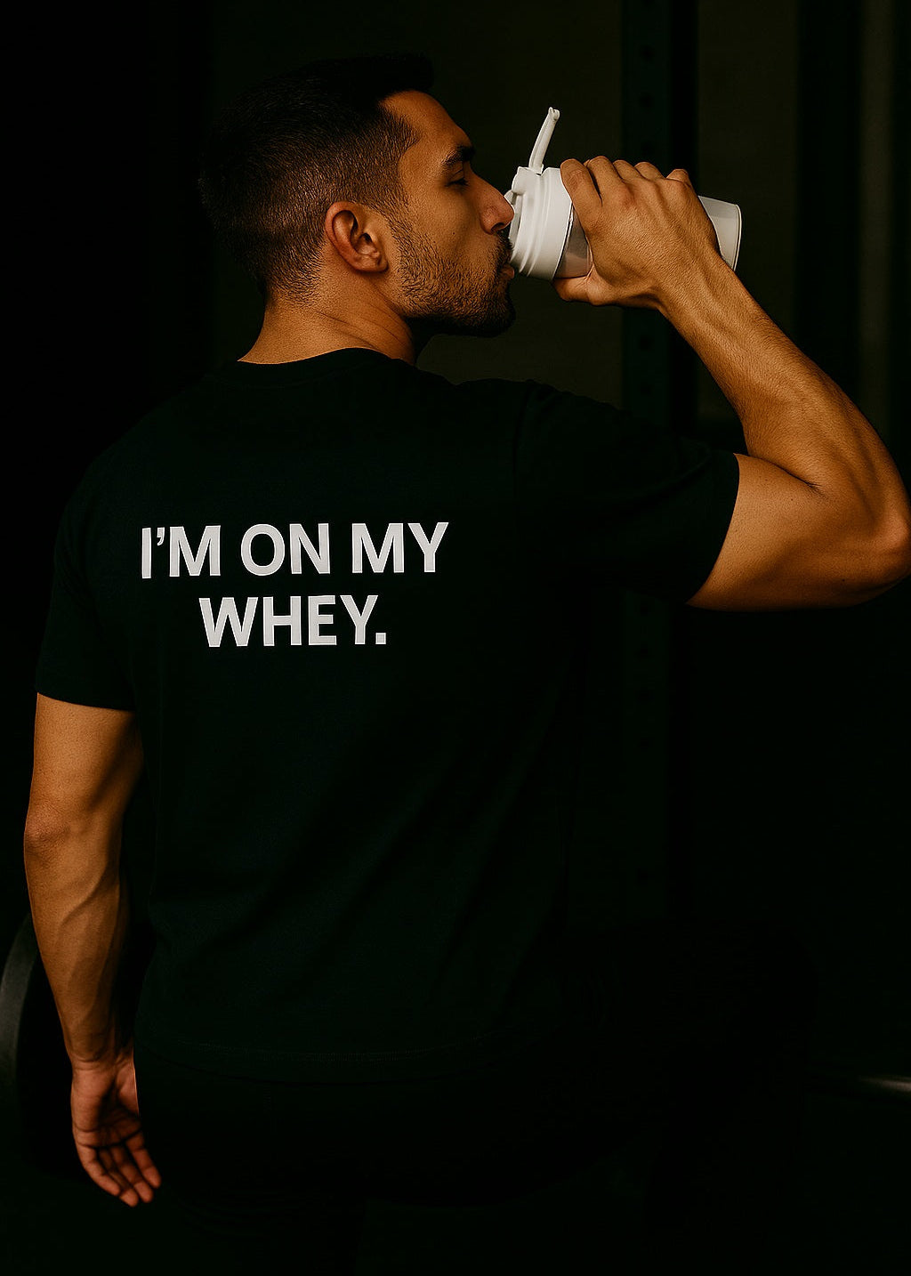 Person wearing a black t-shirt with 'I'm on my whey.' text, holding a white container.