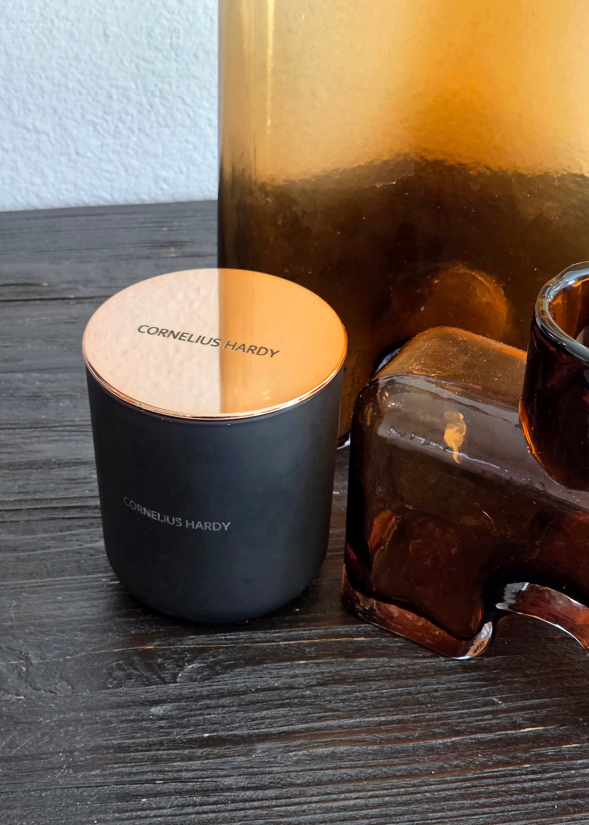 Black candle with gold lid on a wooden surface, next to a glass container.