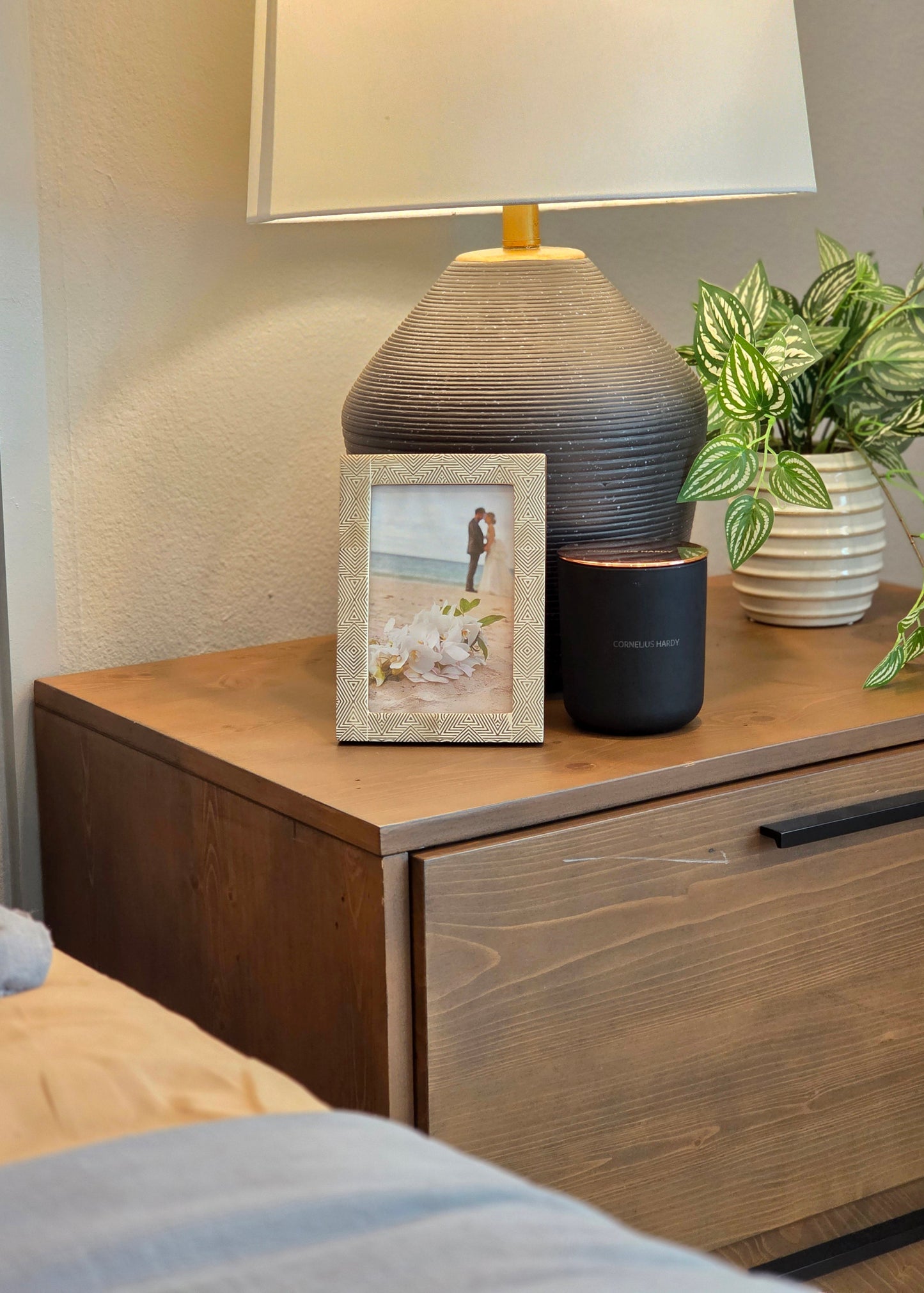 Nighstand with lamp, candle, photo frame, and plant in a bedroom setting