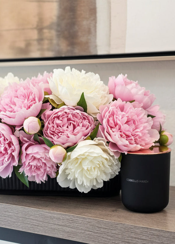 Candle in front of potted plants on a wooden table with a blurred background