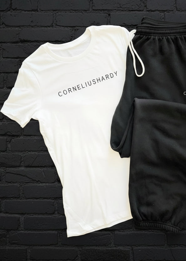 A flat lay of a white crew neck t-shirt with a raised logo and black side-seamed pants, both with 'CORNELIUS HARDY' branding.